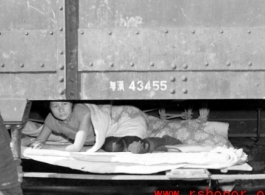 A Chinese refugee has made a tenuous and dangerous bed on the framework hanging below at train car. At the train station in Liuzhou during WWII, in the fall of 1944, as the Japanese advanced during the Ichigo campaign.