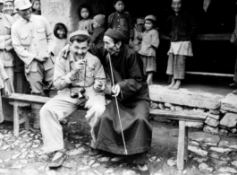 Photographer and funny man Syd Greenberg tries out a long pipe with a local Chinese gentleman, and soldiers and kids look on with enthusiasm, before the Salween River campaign. 