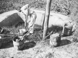 A man collects fertilizer (night soil) from a pit adjacent to farm fields, in preparation for spreading it.