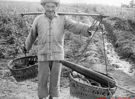 A farmer in Yunnan province carries items in baskets on a shoulder pole. During WWII.