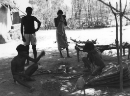 Woman weaves belt of plant fiber (top), men work metal with hand  bellows under a tree (middle), and man gets country haircut in the shade (bottom).  Scenes in India witnessed by American GIs during WWII. For many Americans of that era, with their limited experience traveling, the everyday sights and sounds overseas were new, intriguing, and photo worthy.