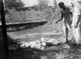 Men look at unfortunate souls, dead from famine, disease, or some other cause.  Scenes in India witnessed by American GIs during WWII. For many Americans of that era, with their limited experience traveling, the everyday sights and sounds overseas were new, intriguing, and photo worthy.