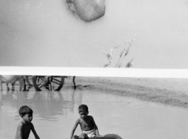 Children riding water buffalo in muddy water.  Scenes in India witnessed by American GIs during WWII. For many Americans of that era, with their limited experience traveling, the everyday sights and sounds overseas were new, intriguing, and photo worthy.