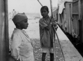 Two boys hang out at train station, one with stalks of sugarcane in hand.  Scenes in India witnessed by American GIs during WWII. For many Americans of that era, with their limited experience traveling, the everyday sights and sounds overseas were new, intriguing, and photo worthy.