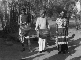 Men with cymbal, drum, and person in a dress.  Scenes in India witnessed by American GIs during WWII. For many Americans of that era, with their limited experience traveling, the everyday sights and sounds overseas were new, intriguing, and photo worthy.