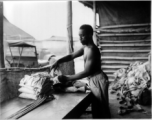 An African-American serviceman carefully packs a parachute for use by aircrews in emergency bailouts, in some location in the CBI where the weather was hot.