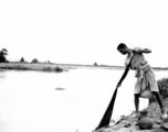 A man fishes with a next from the bank of a river. Probably in India. During WWII.