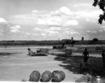 A B-25D of the American 491st Bombardment Squadron is on the taxiway.  Maintenance men who prepared it for the mission stand in the shade of tree. Small bombs, 100 pounds, are seen neatly stacked in the middle of the photo. Closer, in the center, are three 500 pound bombs. They lack the guide fins, and still have the transport 'rings' attached to make it easier to move them around.  Photo believed to have been taken at Yangkai, Yunnan Province, in the spring or summer of 1944. 