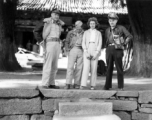 Americans in the China--armed with pistols and cameras--pose under the shade of large ancient trees outside a temple building. During WWII.