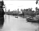 A boat set up to fish using cormorants in a canal in Kunming, while a large group of people have gathered, apparently watching the cormorant fishermen.   In Yunnan province, China, during WW