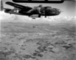 A B-25 Mitchell bomber, #448, in flight and dropping bombs in the CBI, in the area of southern China, Indochina, or Burma.