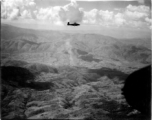 B-25 Mitchell bomber in flight in the CBI, in the area of SW China, Indochina, or Burma. Notice smoke rising in the center. During WWII.