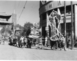 A colorful parade--with floats, marchers, and music--for a local festival in Kunming, China, during WWII.