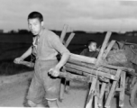 In the near darkness a man in China pulls a cart loaded with benches, an oven in a 55-gallon drum, a scale, and a son--a retail stand or eatery being taken out for a day of work, or being brought back after a day of work. During WWII.