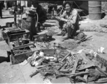 An ironmonger with his wares (including spoons made with the exotic metal aluminum, scavenged from crashed airplanes). Likely in Yunnan province, China, most likely around the Luliang air base area.