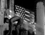 A man fills a bucket, possibly in a water heating facility or kitchen, from a concrete cistern. During WWII.