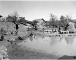 Village scene next to Yangkai, Yunnan province, during WWII, with a pond and people threshing rice. 