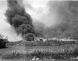 A smoke column arises, and smoke is widely spread about, at an American air base in China during WWII.