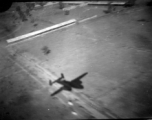 Aerial view of structures and shadow of B-25 in Burma or French Indochina, in the CBI, during WWII.