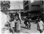 Poor people on street next to nice cars.  Scenes in India witnessed by American GIs during WWII. For many Americans of that era, with their limited experience traveling, the everyday sights and sounds overseas were new, intriguing, and photo worthy.