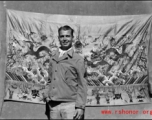 An American serviceman in the CBI, standing in front of an elaborate embroidered silk sheet, during WWII.