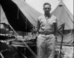 An American stands next to a tent with bed cots, in the CBI, during WWII.