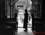 A woman stands in the doorway to a tea house or guild hall or similar meeting place. In Kunming, during WWII.