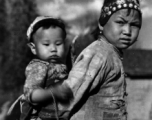 Local people in China: An older sister carries a younger child piggyback as part of her daily responsibilities. During WWII.