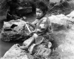Impoverished kid sitting creekside in China during WWII.