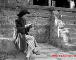 A woman in a maternity dress in a village in Yunnan during WWII. She is likely to be wife of a Nationalist officer, billeted to live in the village, rather than a woman who grew up in the village.