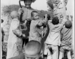 A GI hands out treats (likely candy) to enthusiastic Chinese kids as a farming woman smiles. During WWII.