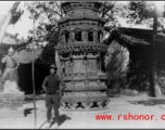 A westerner stands in front of a large incense burner in a temple in China during WWII.