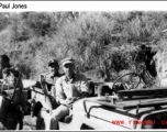 GI and Chinese soldier sit in a jeep, as a worker carries gear during WWII. Probably in Yunnan, China.
