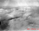 A cloudy landscape below as seen the air from an American bomber (likely a B-25) during WWII.