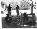 Woman weaves belt of plant fiber (top), men work metal with hand  bellows under a tree (middle), and man gets country haircut in the shade (bottom).  Scenes in India witnessed by American GIs during WWII. For many Americans of that era, with their limited experience traveling, the everyday sights and sounds overseas were new, intriguing, and photo worthy.