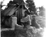 Man squatting on mud wall.  Scenes in India witnessed by American GIs during WWII. For many Americans of that era, with their limited experience traveling, the everyday sights and sounds overseas were new, intriguing, and photo worthy.