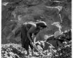 Woman crushes rock by hand, for use in construction.  Scenes in India witnessed by American GIs during WWII. For many Americans of that era, with their limited experience traveling, the everyday sights and sounds overseas were new, intriguing, and photo worthy.